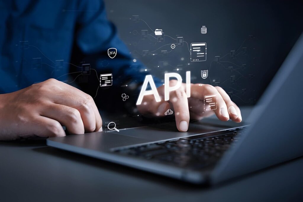 A person in a blue shirt types on a laptop keyboard, with a glowing "API" text and connected icons (security shield, database, documents, files) overlaid above the keyboard, representing API integration and connectivity