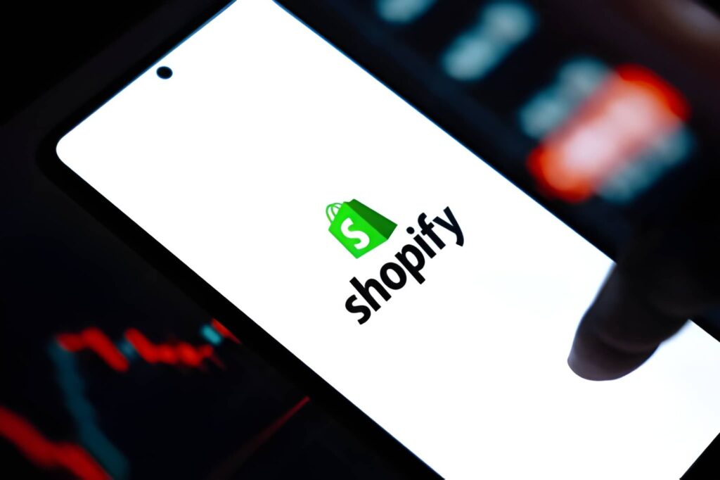 Shopify logo displayed on smartphone screen with financial charts in the background representing eCommerce migration